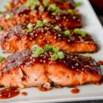 Broiled gochujang salmon fillets with caramelized Korean chili glaze, topped with sesame seeds and sliced green onion on a foil-lined baking sheet