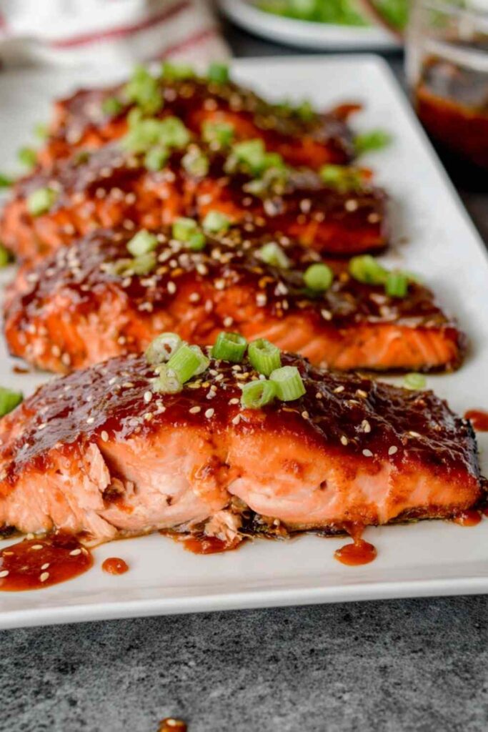 Broiled gochujang salmon fillets with caramelized Korean chili glaze, topped with sesame seeds and sliced green onion on a foil-lined baking sheet