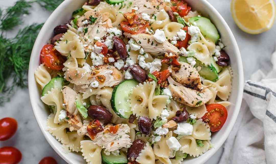 Greek chicken pasta salad with feta cheese, Kalamata olives, cucumber, and cherry tomatoes in a large white bowl