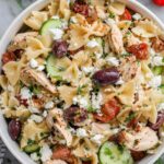 Greek chicken pasta salad with feta cheese, Kalamata olives, cucumber, and cherry tomatoes in a large white bowl