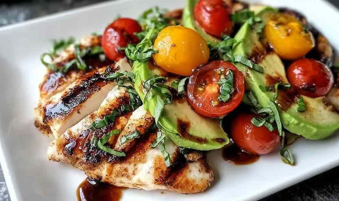Grilled California avocado chicken breast topped with sliced avocado, cherry tomatoes, and melted mozzarella on a white plate