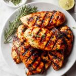 Juicy grilled chicken breast with char marks on a white plate finished with fresh lime and cilantro