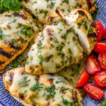 Grilled salsa verde chicken with melted pepper Jack cheese topped with fresh cilantro and lime wedges on a white plate