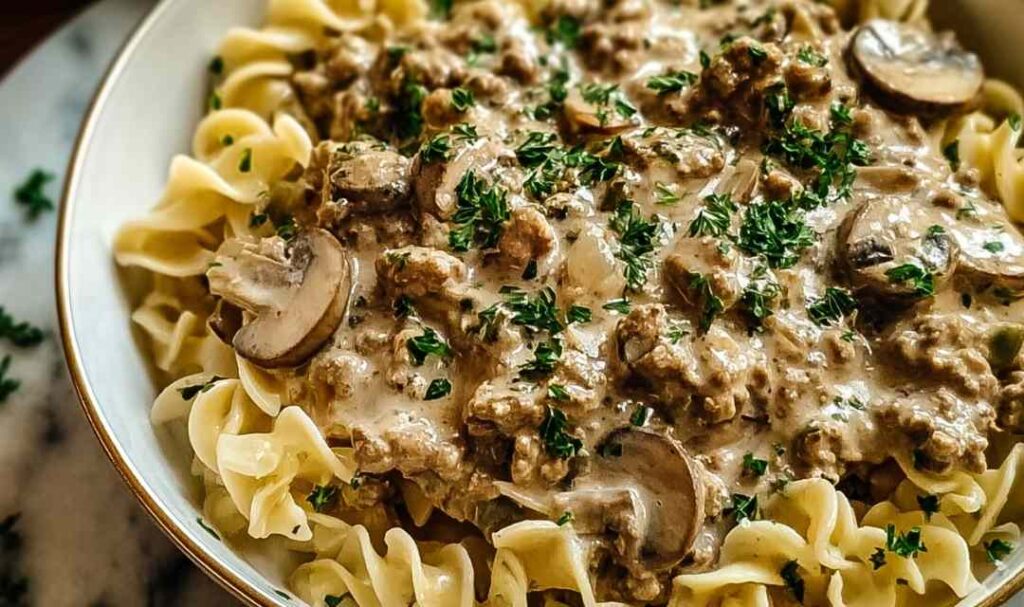 Creamy ground turkey stroganoff served over egg noodles garnished with fresh parsley in a white bowl