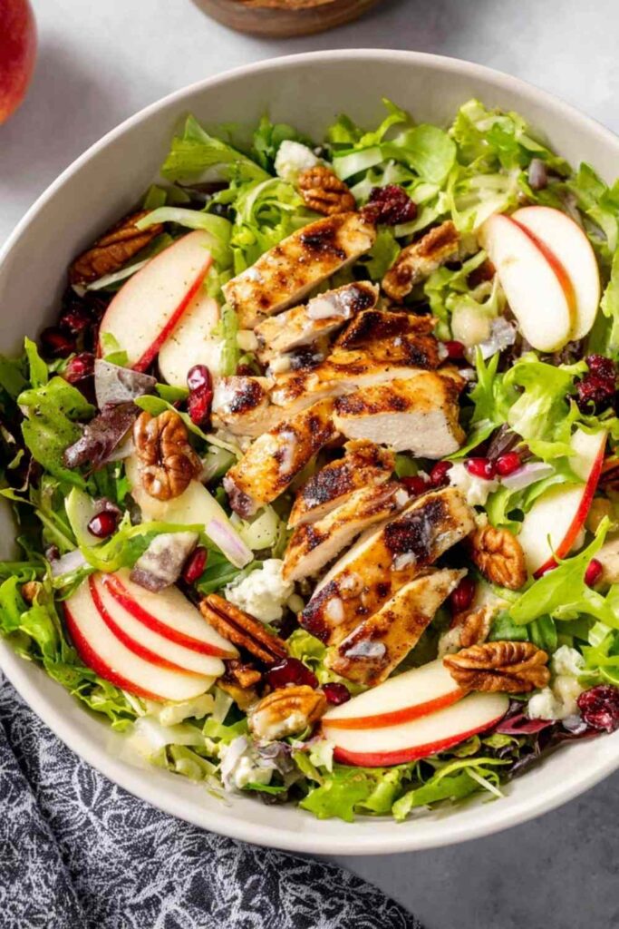Fall harvest chicken salad with grilled chicken, apple slices, pecans, cranberries, and maple Dijon dressing in a white bowl