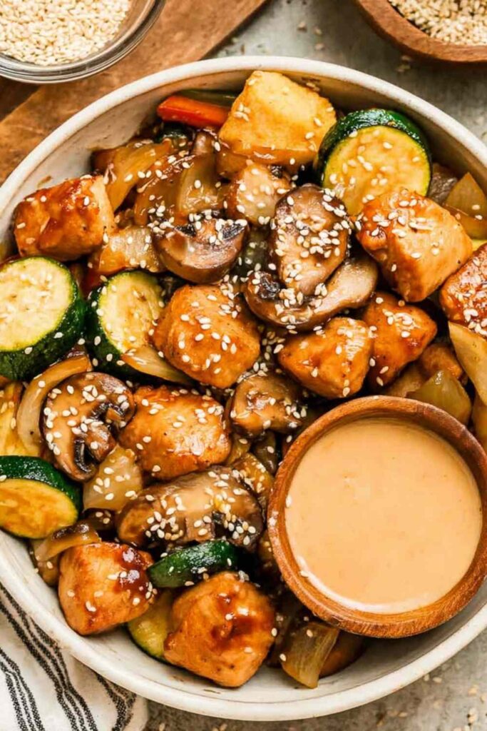 Hibachi chicken and vegetables in a skillet with golden seared chicken breast pieces, zucchini, mushrooms, carrots, and onion