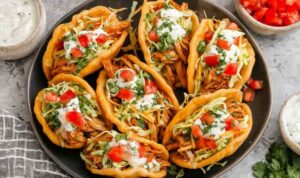 Crispy homemade chicken chalupas filled with seasoned chicken, shredded cheese, lettuce, and diced tomatoes on a wooden serving board