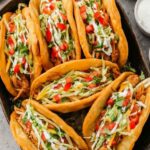 Crispy homemade chicken chalupas filled with seasoned chicken, shredded cheese, lettuce, and diced tomatoes on a wooden serving board