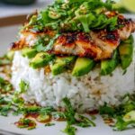Honey lime chicken avocado rice stack on a white plate topped with fresh cilantro and lime dressing