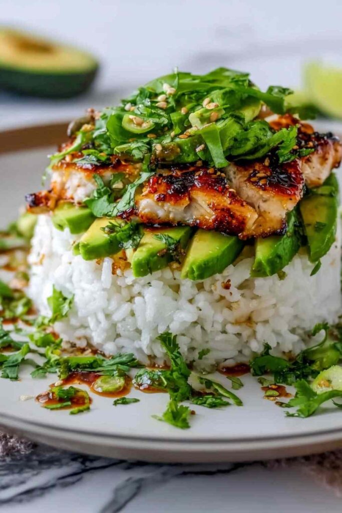 Honey lime chicken avocado rice stack on a white plate topped with fresh cilantro and lime dressing