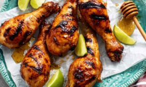Grilled honey lime chicken drumsticks with reduced glaze on a white serving plate with lime wedges