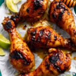 Grilled honey lime chicken drumsticks with reduced glaze on a white serving plate with lime wedges