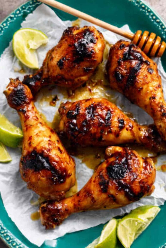 Grilled honey lime chicken drumsticks with reduced glaze on a white serving plate with lime wedges