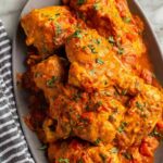 Creamy chicken paprikash in a white bowl over buttered egg noodles garnished with fresh parsley