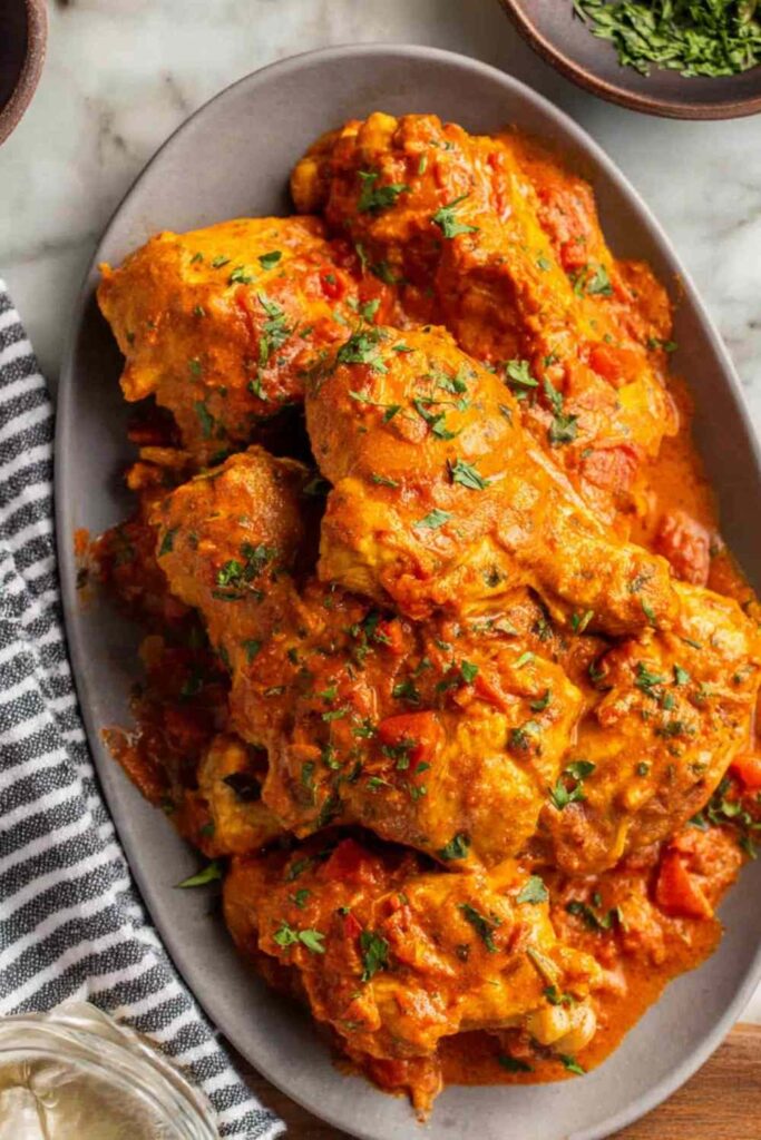 Creamy chicken paprikash in a white bowl over buttered egg noodles garnished with fresh parsley