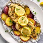 Lemon chicken foil packet opened on a baking sheet showing juicy Italian-seasoned chicken breast with buttery baby potatoes and lemon rounds