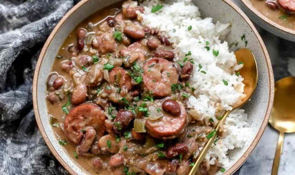 Bowl of Louisiana red beans and rice with chicken andouille sausage, smoky bacon, and kidney beans served over white rice with green onion garnish