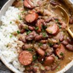 Bowl of Louisiana red beans and rice with chicken andouille sausage, smoky bacon, and kidney beans served over white rice with green onion garnish