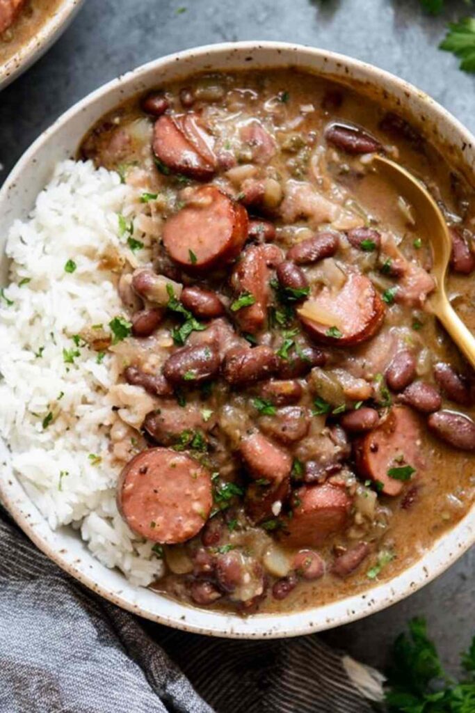 Bowl of Louisiana red beans and rice with chicken andouille sausage, smoky bacon, and kidney beans served over white rice with green onion garnish