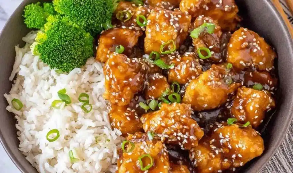 Mandarin chicken recipe in a skillet with glossy orange sauce coating golden browned chicken breast cubes