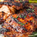 Bone-in grilled chicken thighs with crispy golden skin cooking on a grill grate