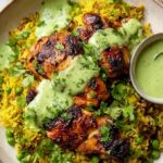 Peruvian chicken and rice with green sauce served in a bowl with sliced avocado and fresh lime wedges