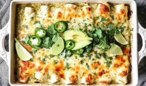 Creamy salsa verde chicken enchiladas baked golden and bubbly in a white casserole dish topped with fresh cilantro and sliced jalapenos