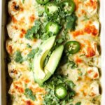 Creamy salsa verde chicken enchiladas baked golden and bubbly in a white casserole dish topped with fresh cilantro and sliced jalapenos
