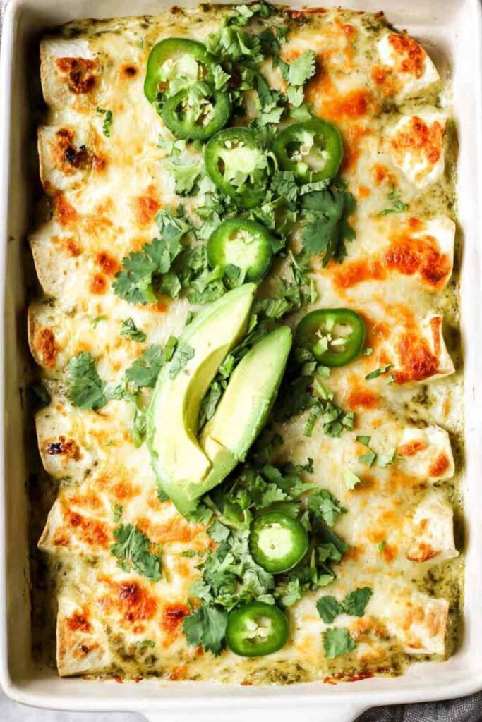 Creamy salsa verde chicken enchiladas baked golden and bubbly in a white casserole dish topped with fresh cilantro and sliced jalapenos