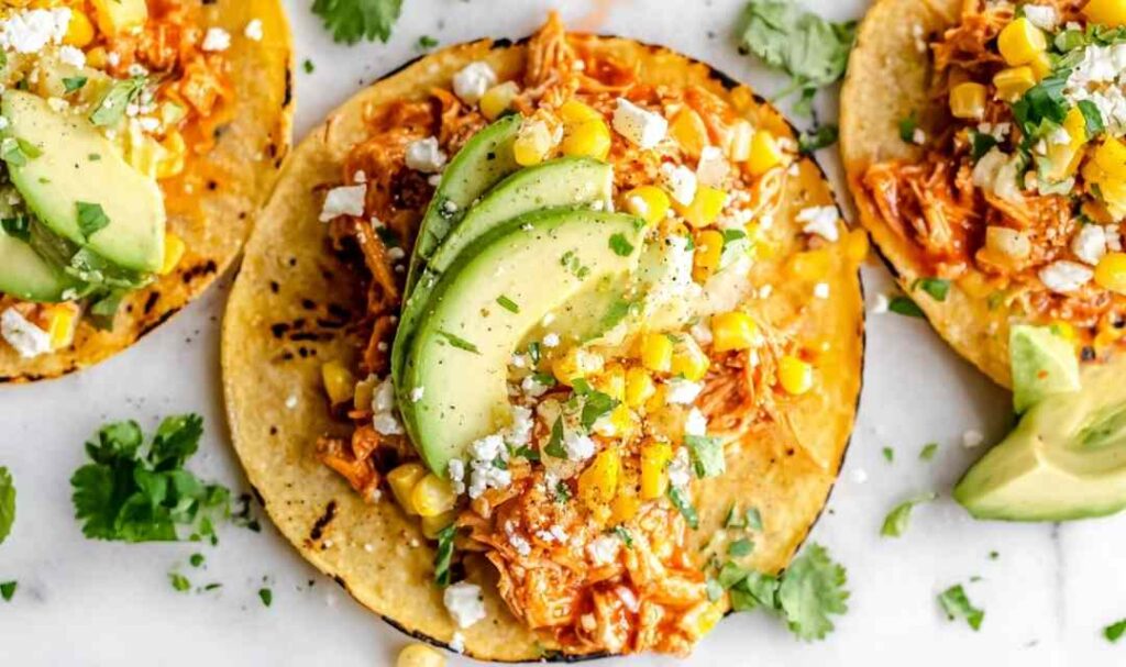 Shredded Chipotle Chicken Tacos 5 Shredded chipotle chicken tacos on charred corn tortillas topped with avocado, sweet corn, cilantro, and cotija cheese