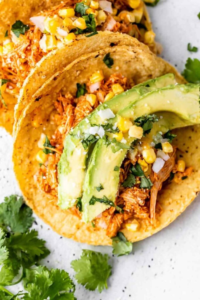 Shredded Chipotle Chicken Tacos 6 Shredded chipotle chicken tacos on charred corn tortillas topped with avocado, sweet corn, cilantro, and cotija cheese