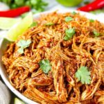 Shredded Mexican chicken in smoky chipotle tomato sauce served in a white bowl with lime and cilantro