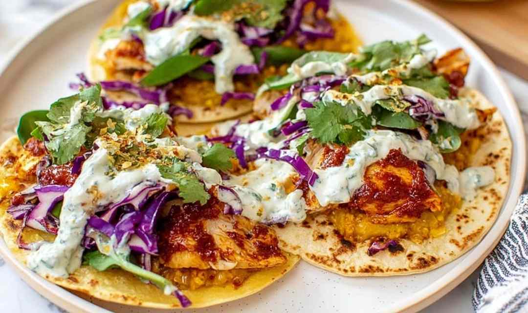 Smashed chicken tacos in warm corn tortillas topped with shredded lettuce, diced tomatoes, and fresh lime wedges served on a wooden board