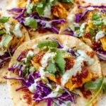 Smashed chicken tacos in warm corn tortillas topped with shredded lettuce, diced tomatoes, and fresh lime wedges served on a wooden board