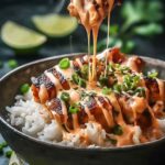 Sweet chili chicken bowl with coconut lime drizzle, jasmine rice, edamame, cucumber, and sesame seeds in a white bowl