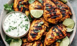 Grilled tandoori chicken marinade served on a white plate with warm naan and raita dipping sauce