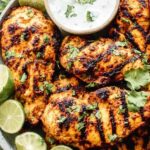 Grilled tandoori chicken marinade served on a white plate with warm naan and raita dipping sauce