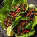 Thai Basil Beef Lettuce Cups served on a rustic wooden board with fresh basil and lime wedges