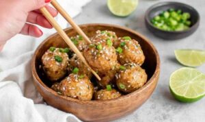 Thai chicken meatballs with sweet chili sauce garnished with green onions and sesame seeds on a white plate