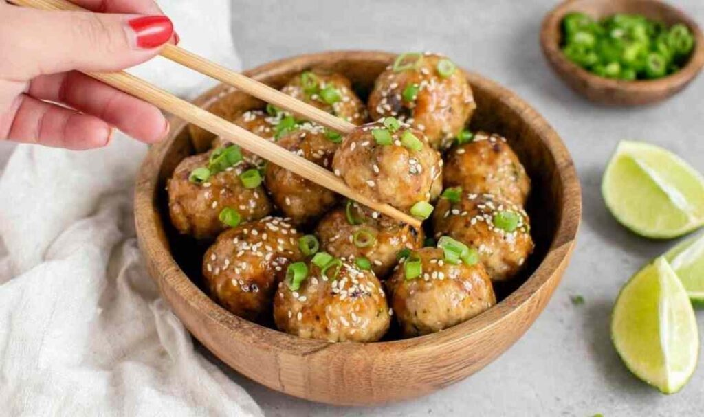 Thai chicken meatballs with sweet chili sauce garnished with green onions and sesame seeds on a white plate