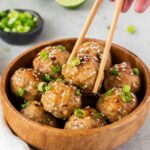 Thai chicken meatballs with sweet chili sauce garnished with green onions and sesame seeds on a white plate
