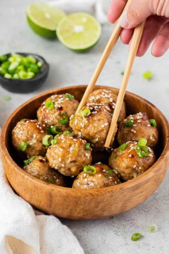 Thai chicken meatballs with sweet chili sauce garnished with green onions and sesame seeds on a white plate