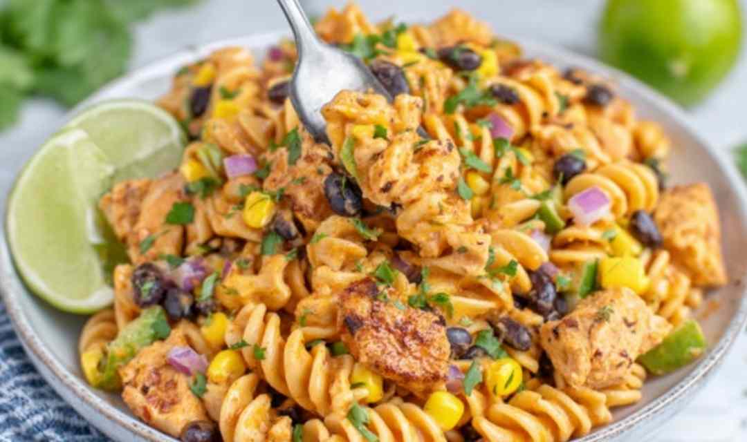 Zesty Chicken Enchilada Pasta Salad in a large white bowl topped with cheddar cheese, fresh cilantro, and crushed tortilla chips