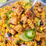Zesty Chicken Enchilada Pasta Salad in a large white bowl topped with cheddar cheese, fresh cilantro, and crushed tortilla chips