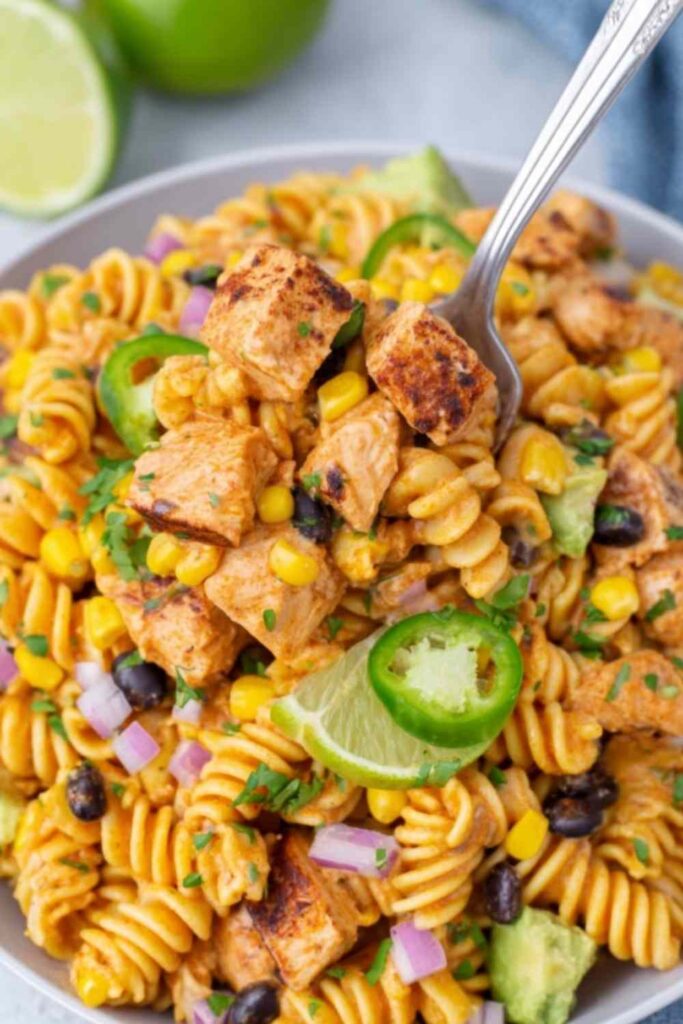 Zesty Chicken Enchilada Pasta Salad 6 Zesty Chicken Enchilada Pasta Salad in a large white bowl topped with cheddar cheese, fresh cilantro, and crushed tortilla chips