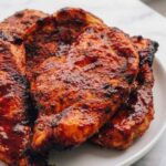 Juicy air fryer BBQ chicken breast sliced on a white plate with sticky BBQ glaze and dipping sauce on the side