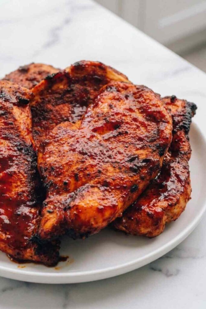 Juicy air fryer BBQ chicken breast sliced on a white plate with sticky BBQ glaze and dipping sauce on the side