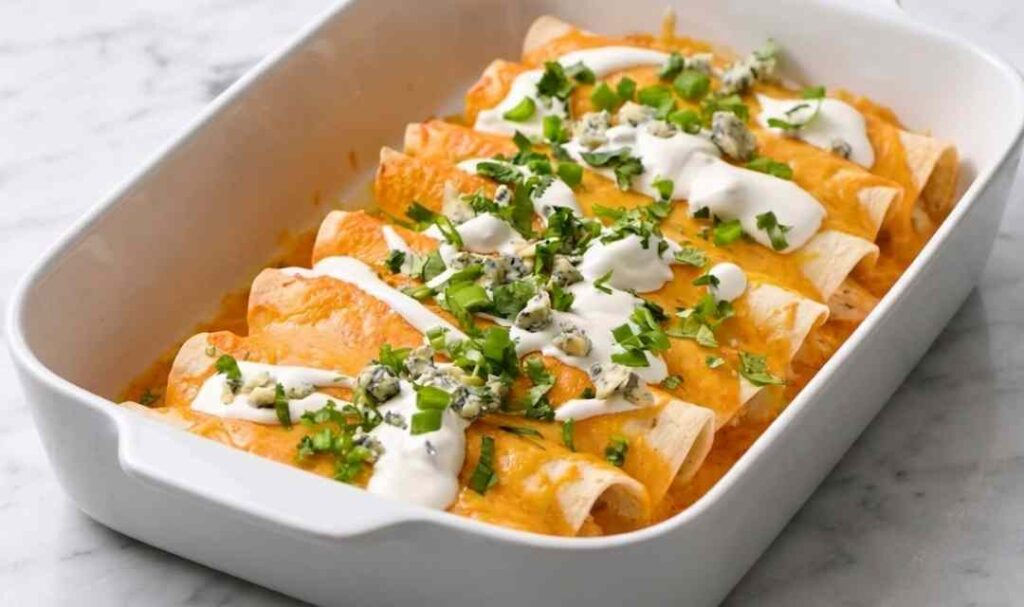 Cheesy baked buffalo chicken enchiladas in a 9x13 pan drizzled with ranch and topped with green onions