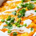 Cheesy baked buffalo chicken enchiladas in a 9x13 pan drizzled with ranch and topped with green onions