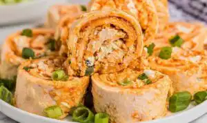 Buffalo Chicken Pinwheels Buffalo Chicken Pinwheels arranged on a white serving platter with celery sticks and blue cheese dipping sauce on the side